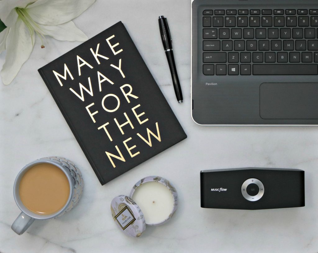 Flat lay of journal, pen, coffee, candle, laptop, and speaker.