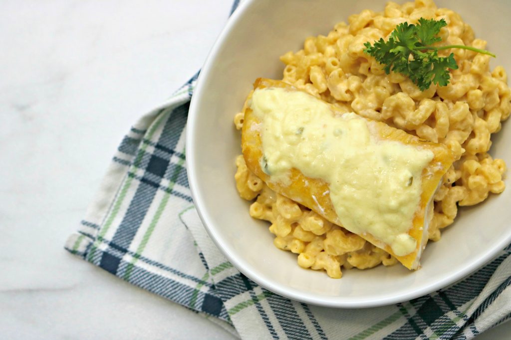 A bowl of mac and cheese topped with parsley and white and flaky fish with a cheese sauce. 