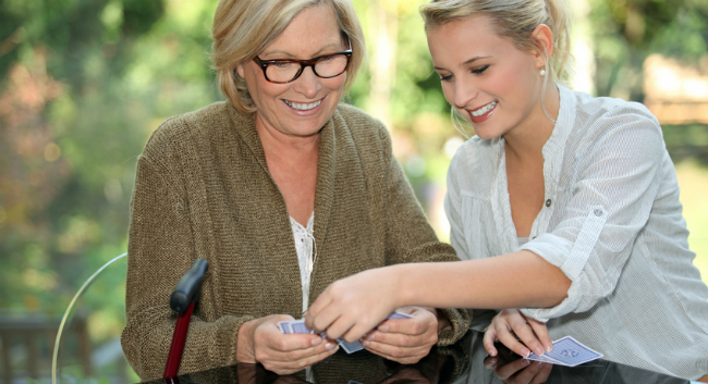 A woman plays cards with the a senior.