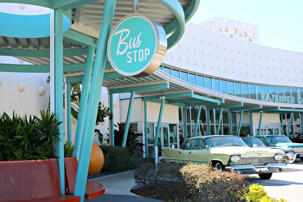 A line up of vintage cars lines the parking spaces and a vintage bust stop signs is in focus. 