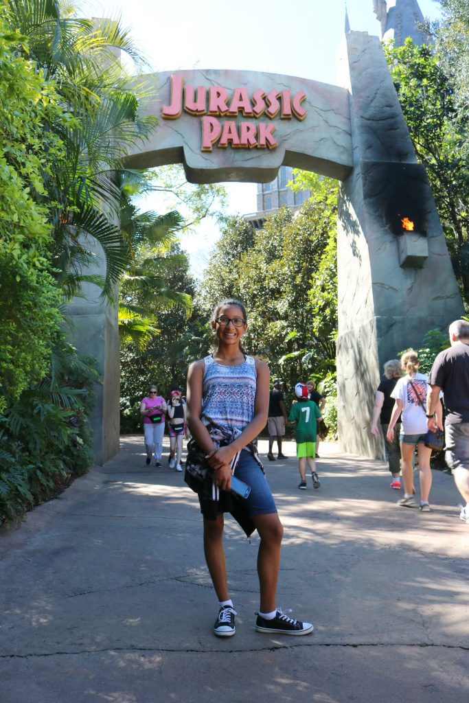 A girl stands in front of the Jurassic Park gate.