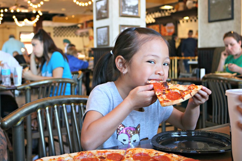 Little girl bites into a big slice of pizza at a restaurant at Universal Studios. 