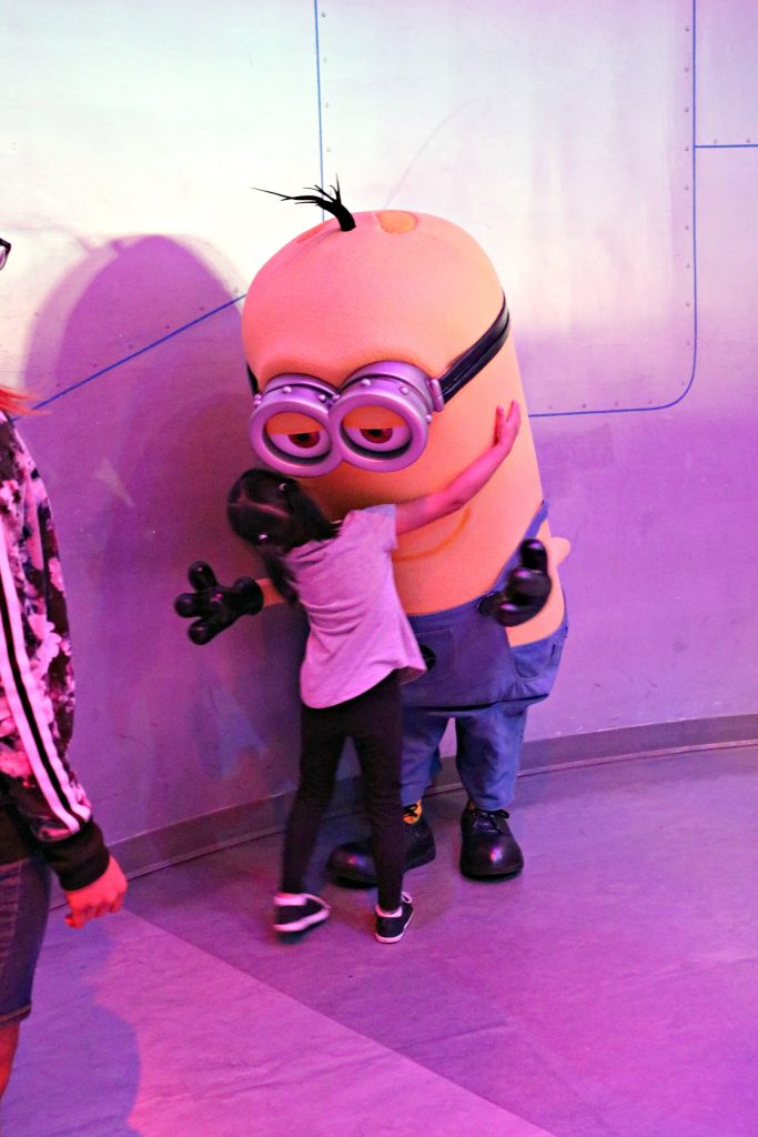 A little girl hugs a minion from Despicable Me. 