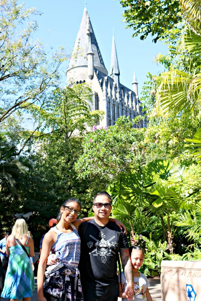 Two girls and her dad pose at Universal Studios, Hogwarts Castle is seen in the distance.