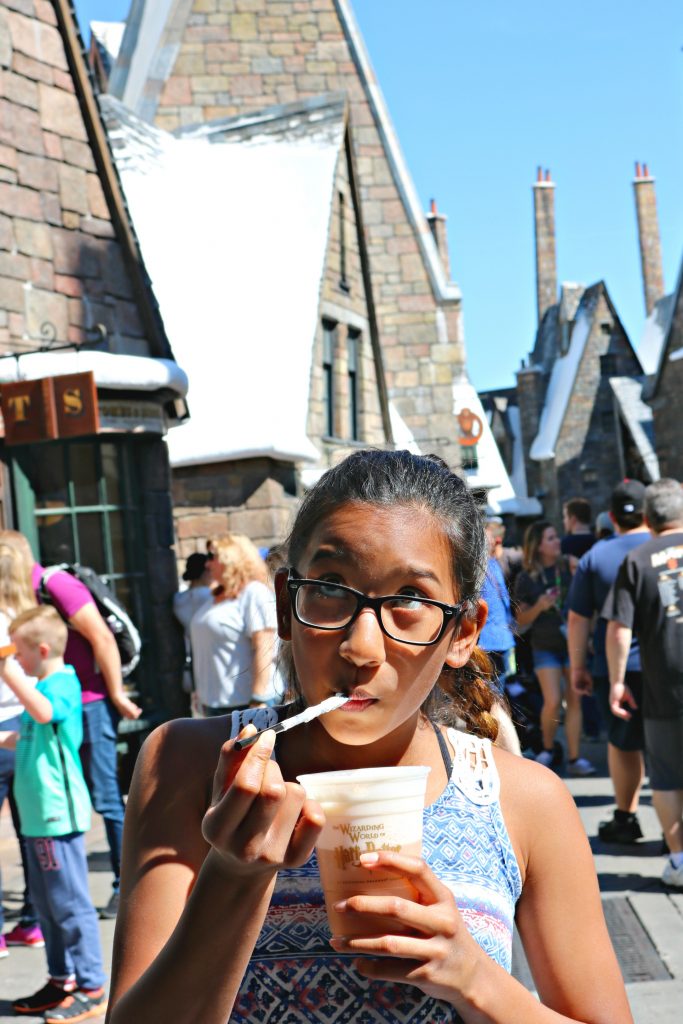 Girl puts straw in her mouth to enjoy the foam of butterbeer at Hogsmeade. 