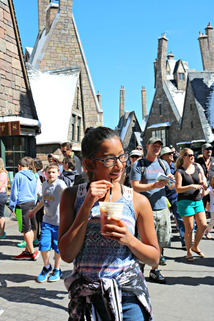 Girl stands in the center of Hogsmeade drinking butterbeer. 