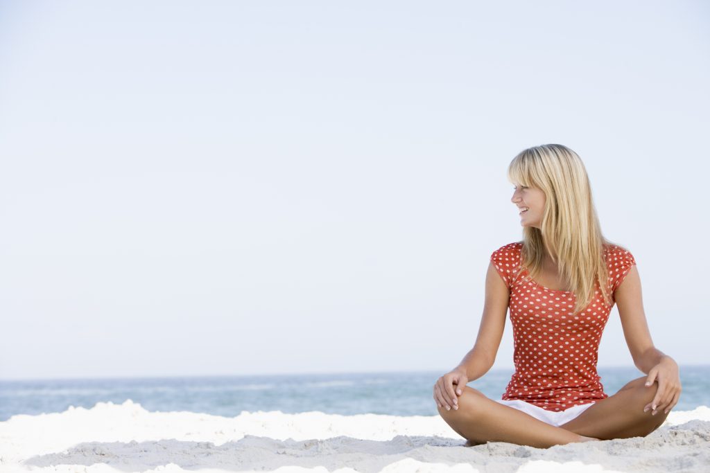 Woman sits on a beach, she looks to her right.