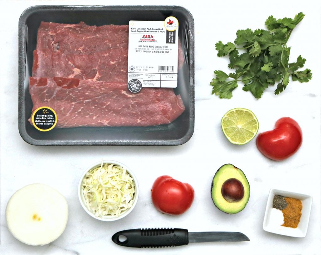 Cooking ingredients flat lay of beef, cilantro, onion, tomatio, avocado, spices, and more.