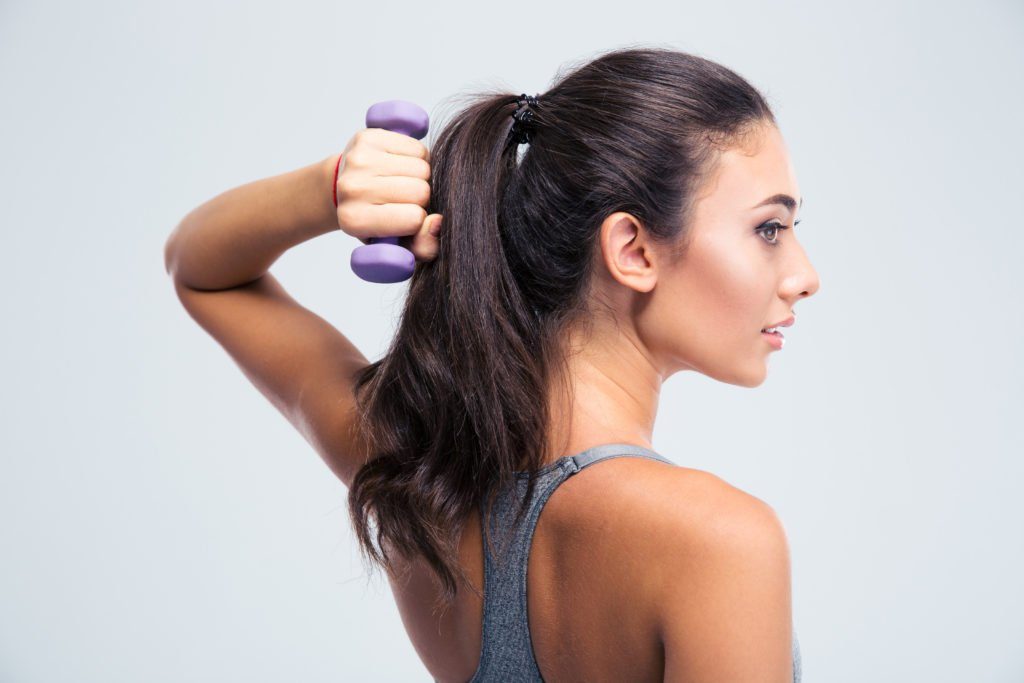 Side view portrait of a beautiful sports woman working out with dumbbells isolated on a white background.