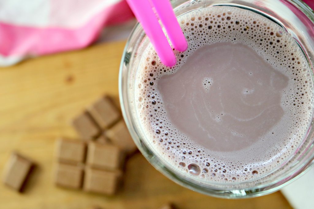 Top view of Equate shake, with two straws. On the wooden board below, there's a chocolate split in half.