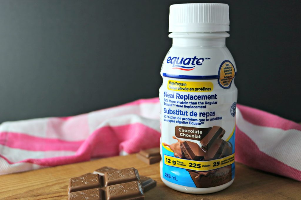 Equate Meal Replacement, in Chocolate flavour. There's a striped white and pink napkin behind it, on a wooden board with chunks of chocolate. 