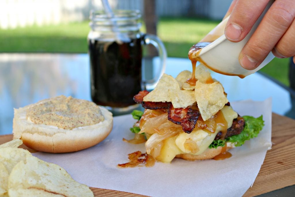 Darasak pours gravy over Bacon Poutine burger. It's a setting outdoors, soda is in the background.