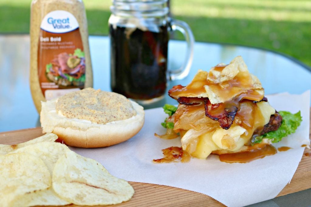 The burger sits with the top bun off and shows all the topping dripping onto wax paper. Served with a soda and chips.