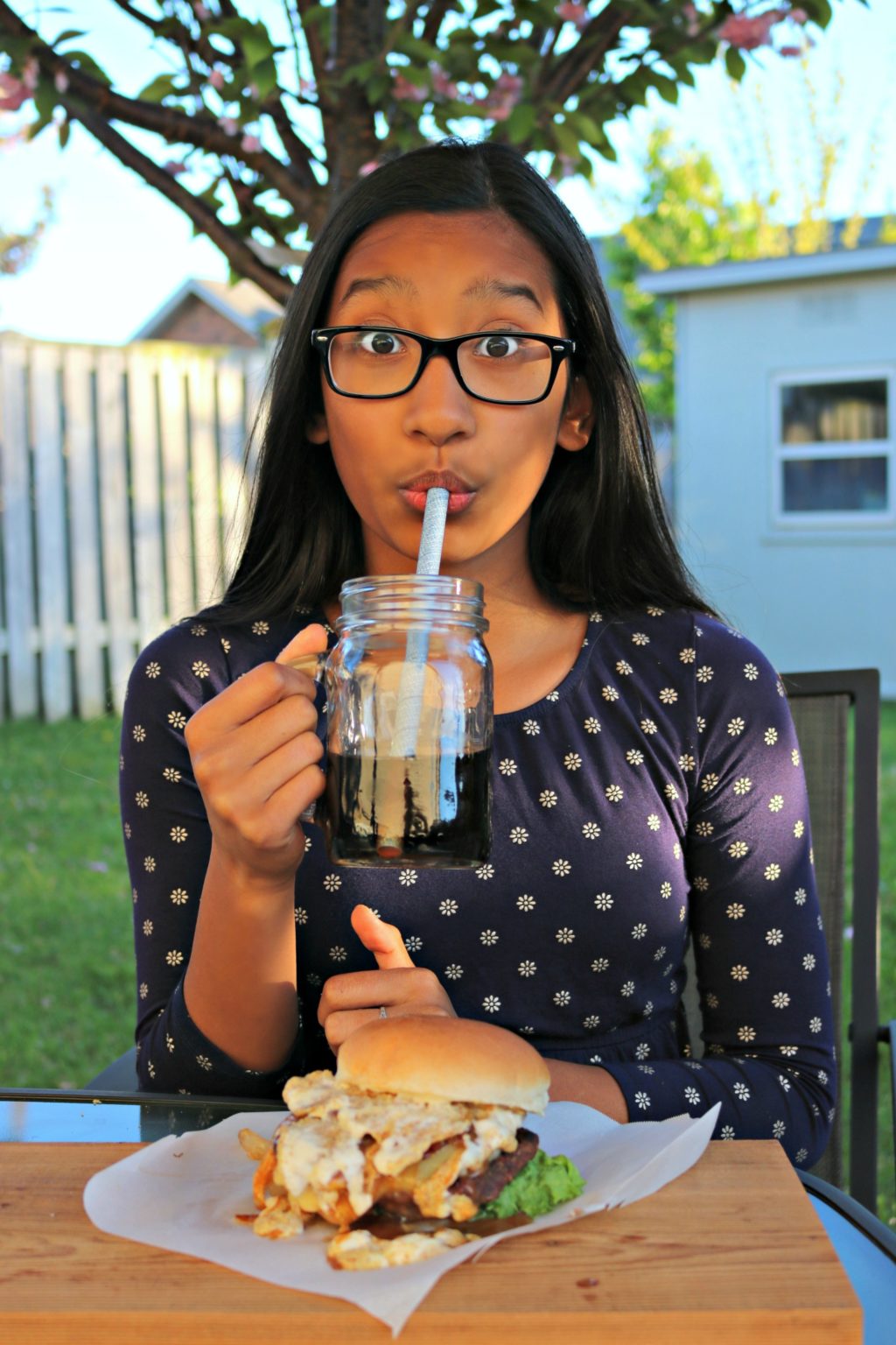 Gabby take a sip of her soda, her eyebrows are raised in shock at how good the burger is.