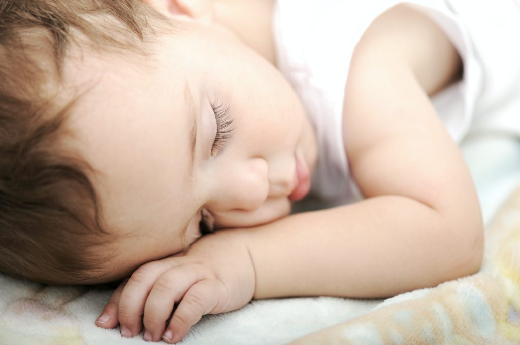 A baby sleeps on his stomach. The baby looks peaceful and has long eyelashes.