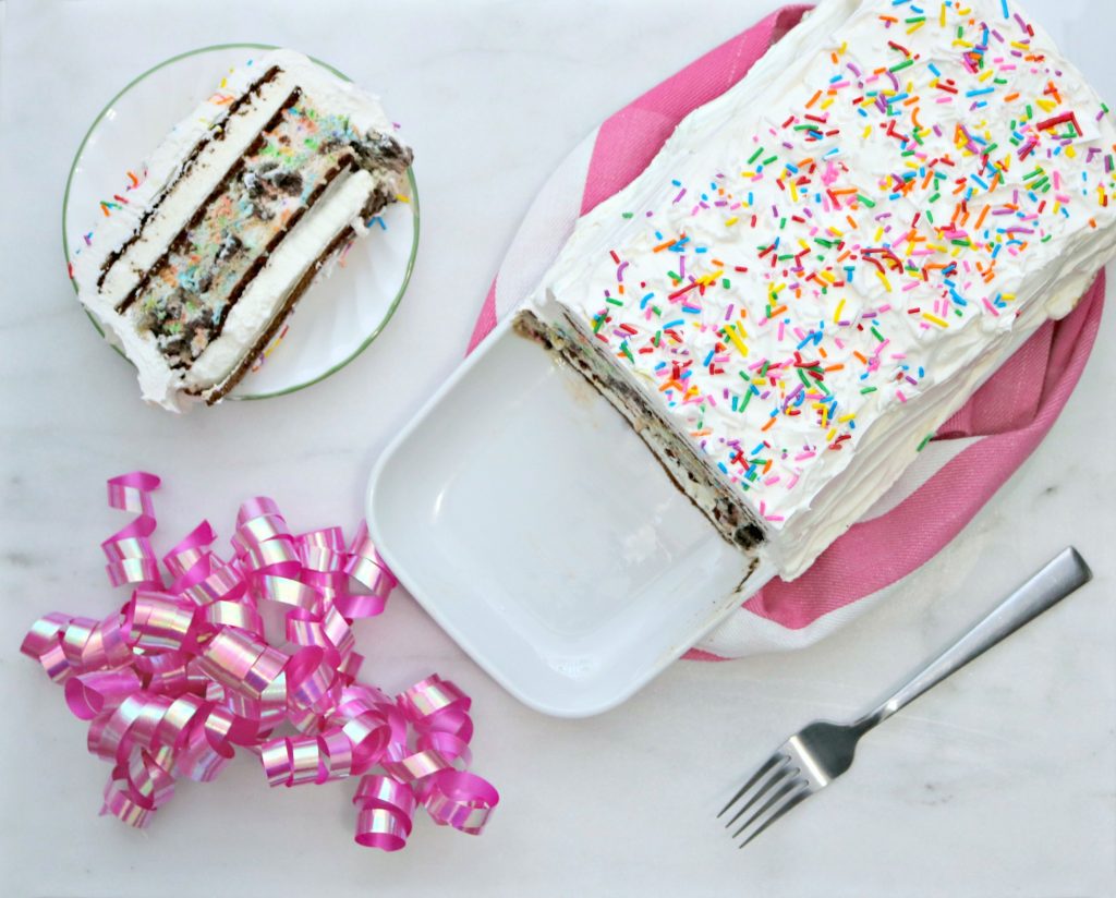 Final product of the easy ice cream cake, top view with a slice cut out. Slice on a small plate surrounded by a pink ribbon and fork. 