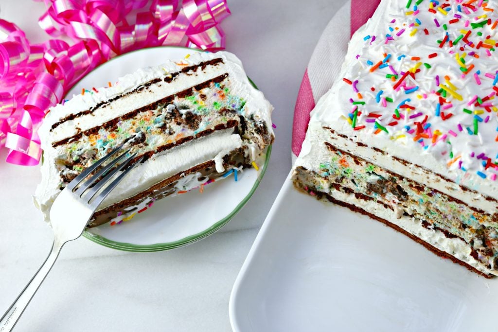 Easy icecream cake on a long pan with a slice with a fork on a small plate. Pink ribbon is in the background. 