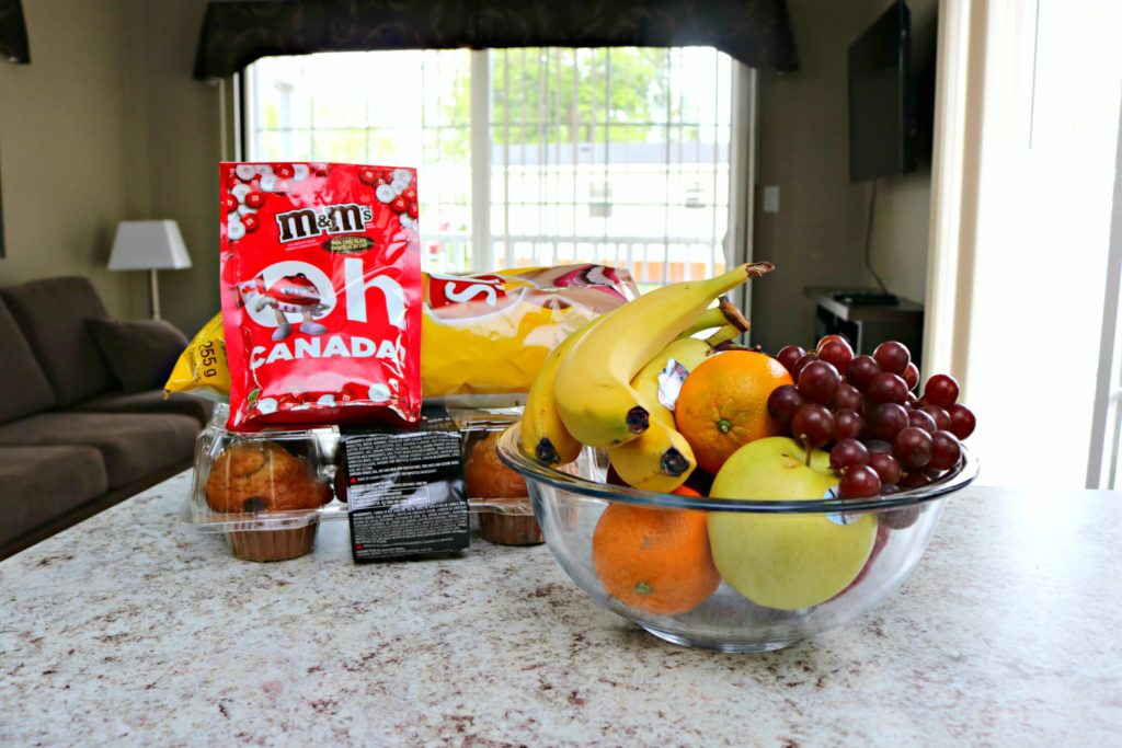 A basket of goodies, fruits, and chocolates are shown on the kitchen counter.