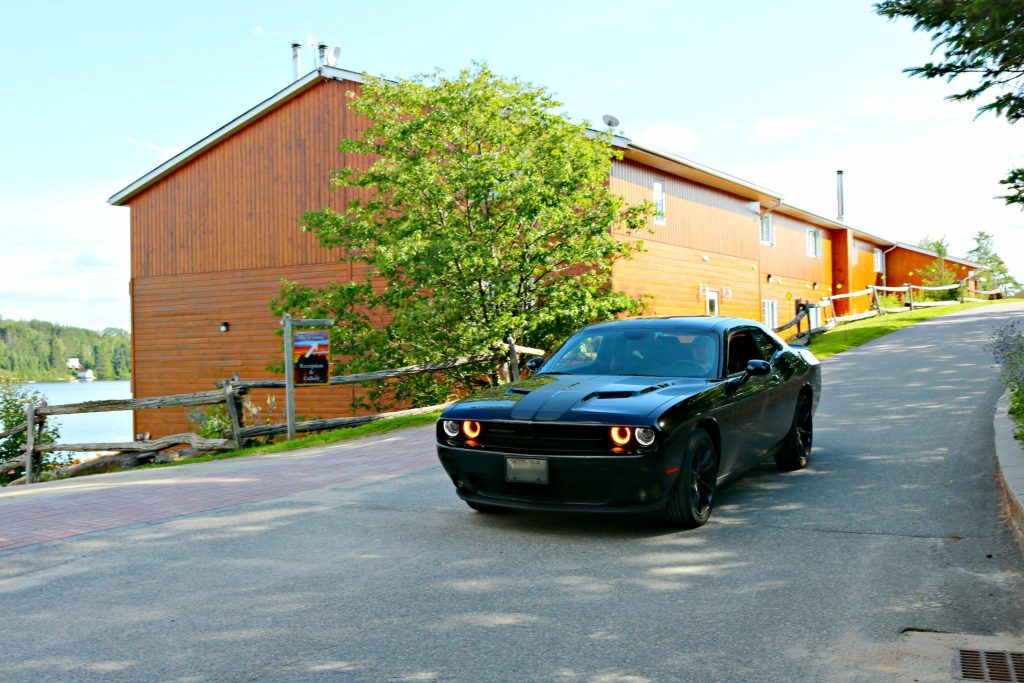 A Dodge Challenger is pictured coming down the drive, cabins are pictured behind it. 