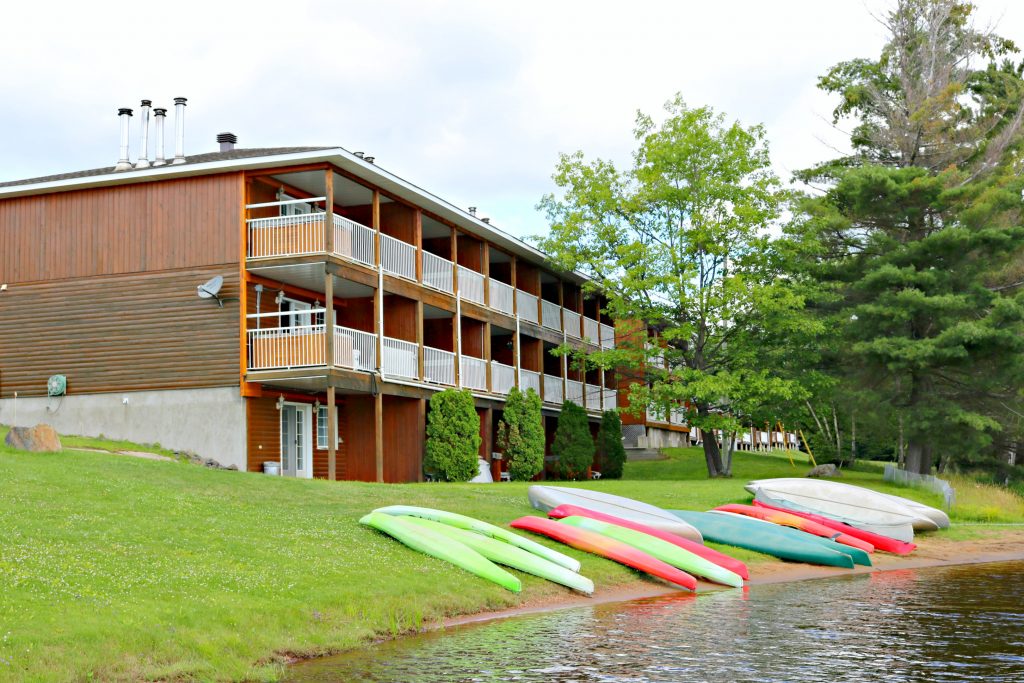 A building with balconies with private hot tubs are shown. It is right by the water and canoes are docked. 