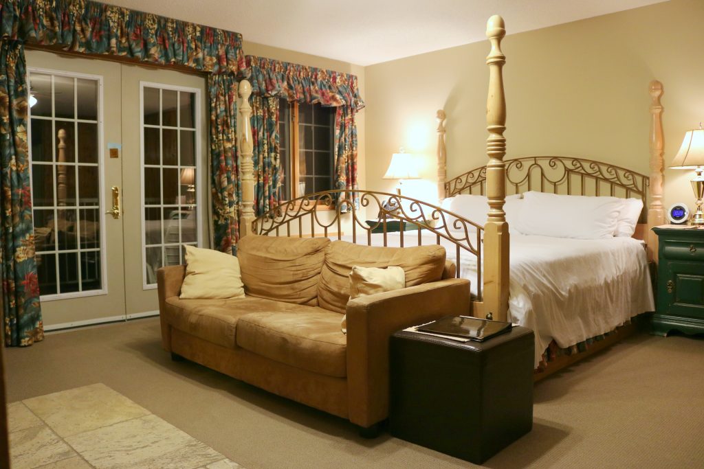 A beautiful king size bed is shown with a loveseat at the end of the bed. It's styled in a traditional old world style. 