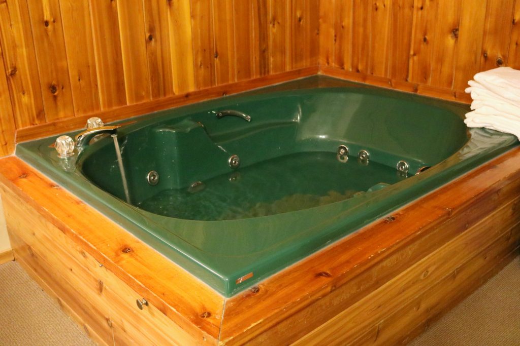 An indoor hot tub is being filled and is surrounded by wooden planks. 