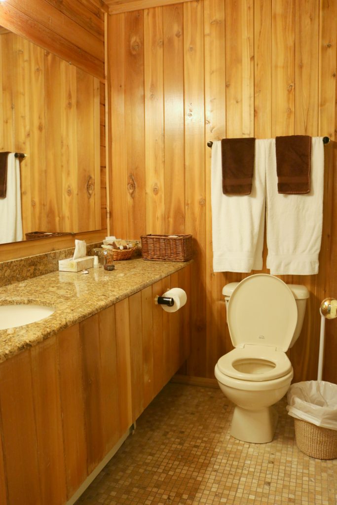 The bathroom is wooden blanks also, very rustic and a toilet and sink are shown. 