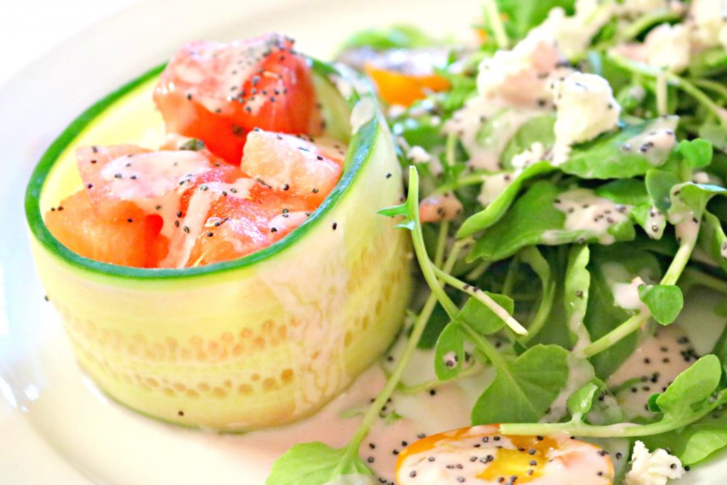 A cucumber slice made into a bowl with diced watermelon with a side of green salad. 