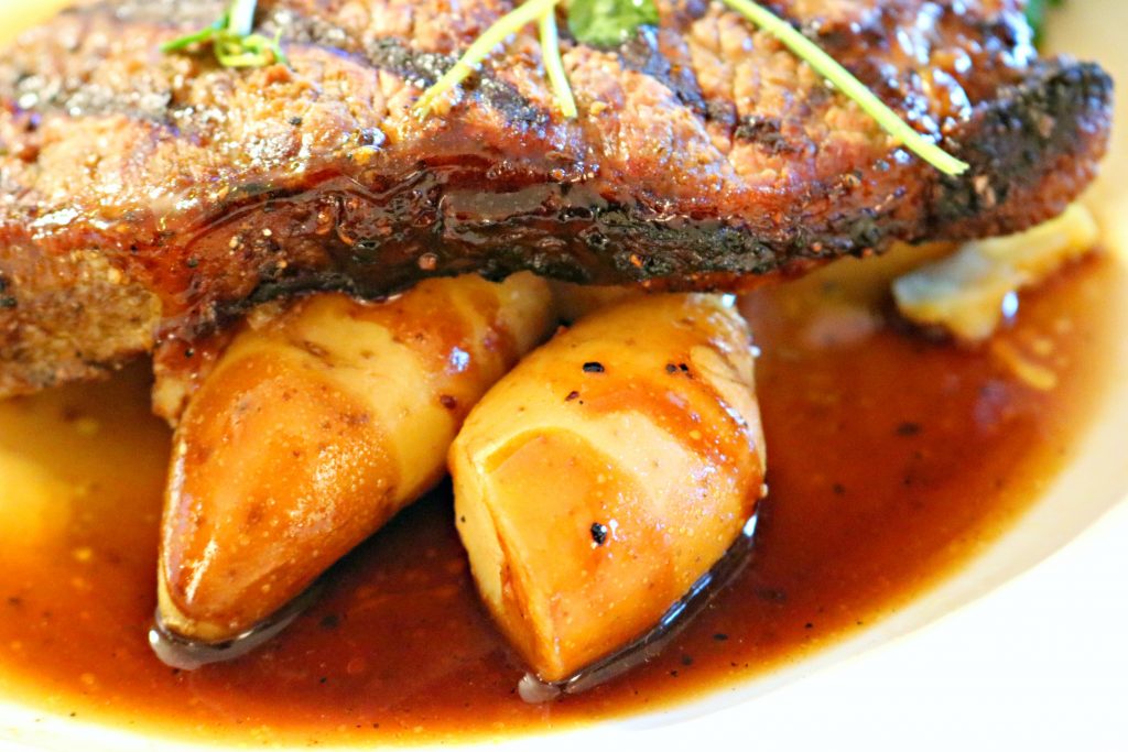 A perfectly grilled steak is placed on fingerling potatoes in aus jus. 