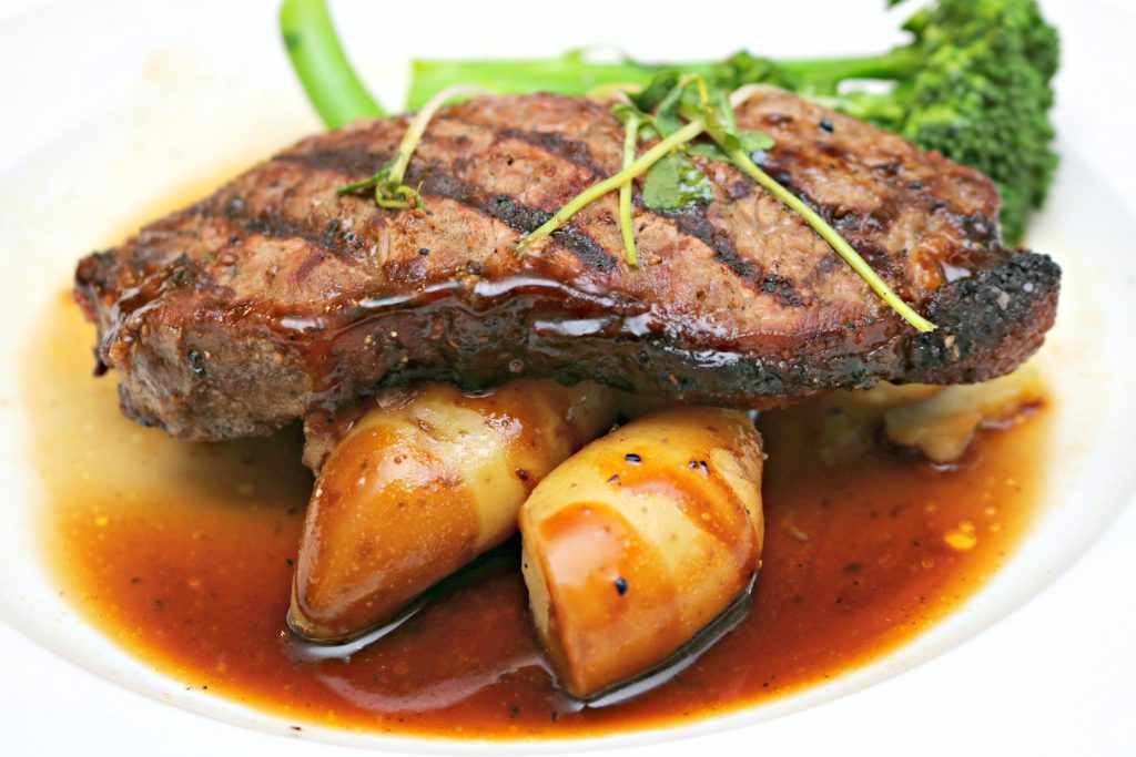 A full picture of steak with fingerling potatoes, broccolini, and aux jus.