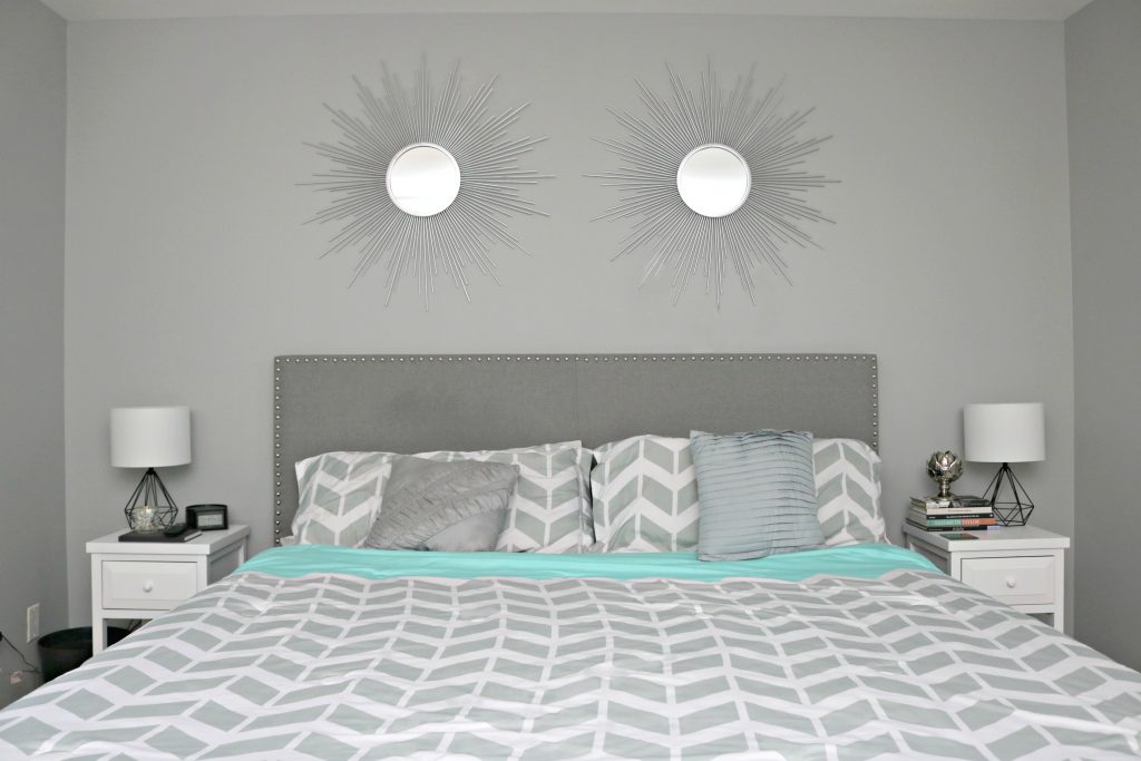 The bed is shown with herringbone sheets in grey and teal, with decorative pillows and two night stands. 