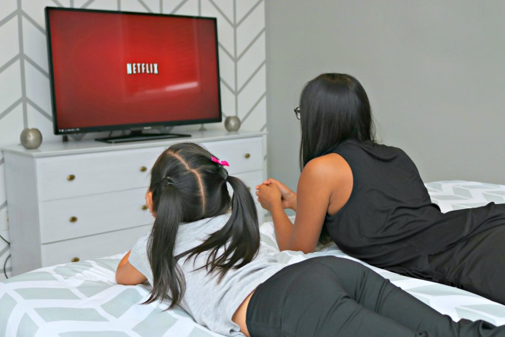 Two girls lay on their tummies and watch the screen as Netflix loads. 