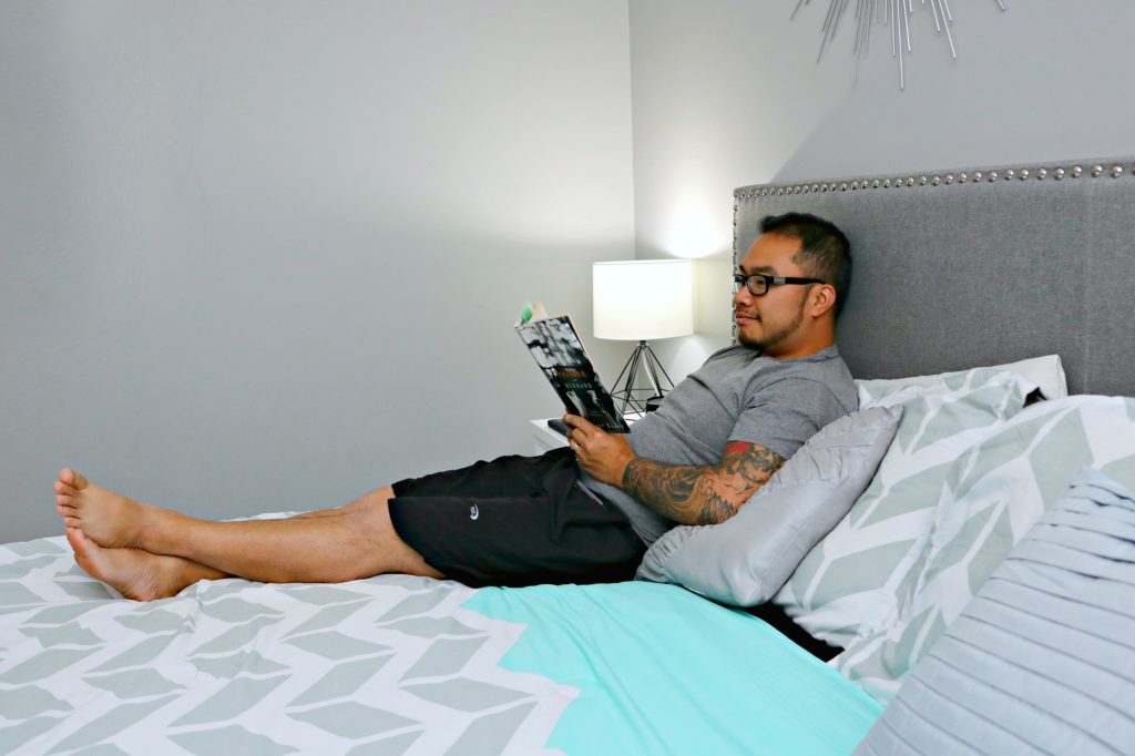 A man reads a book and lies in his bed relaxing. 