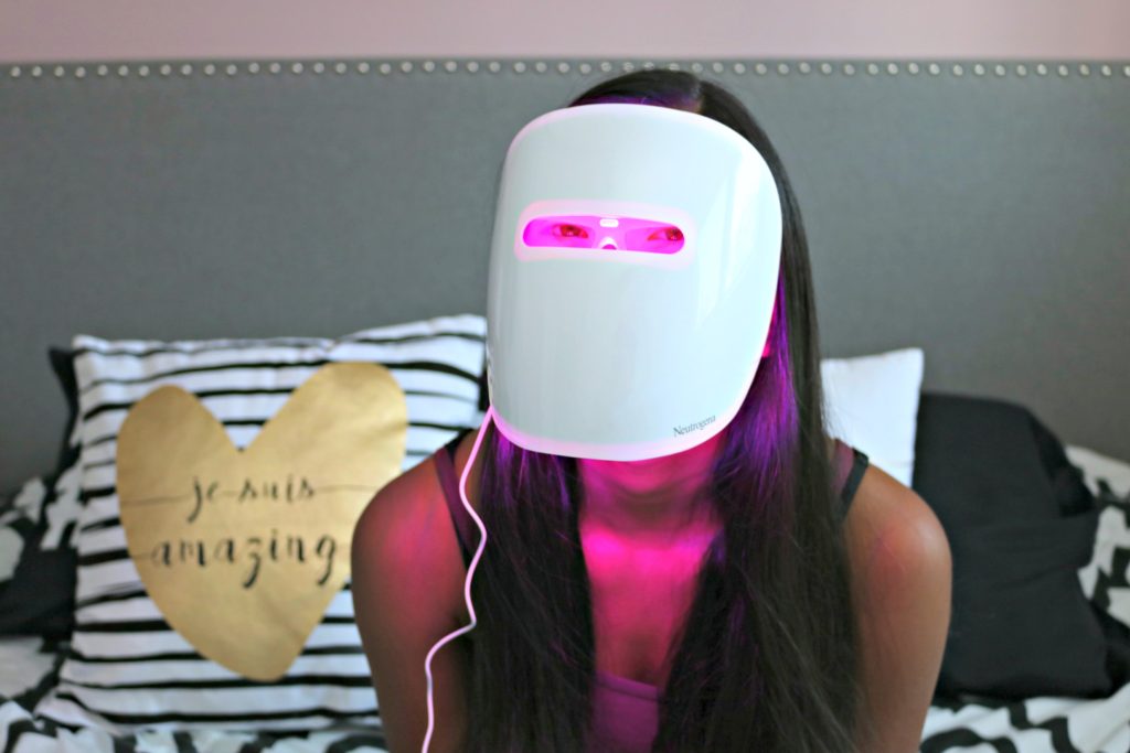 Gabby wearing the Neutrogena Acne Light Therapy mask, her eyes are visible underneath the pink light. 