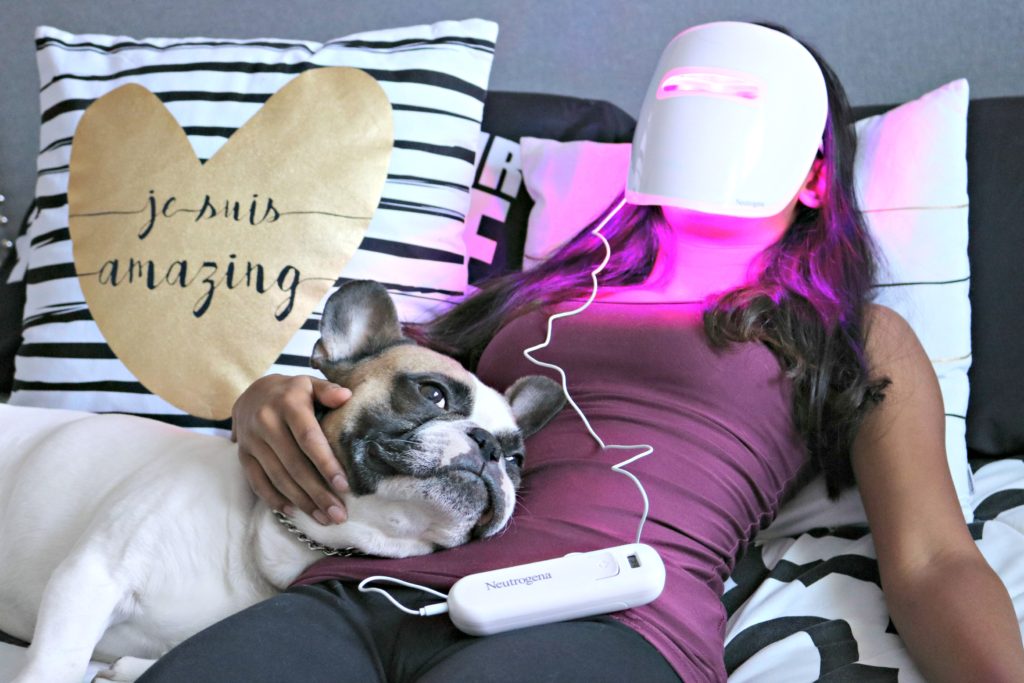 Gabby lays with Maverick the French in bed while she wears the Neutrogena Acne Light Mask. 