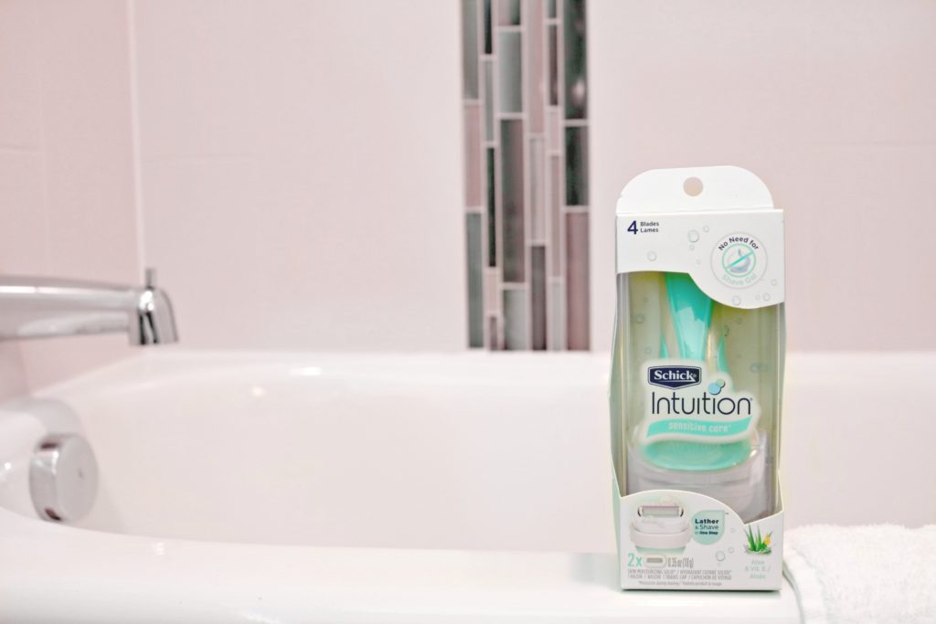 A teal Schick Intuition razor sits on a bath tub, ready to be used. 