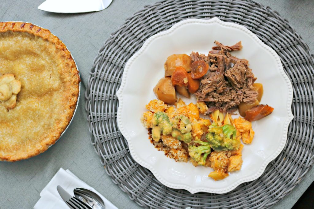 Top view of roast beef with potatoes, carrots, and mac and cheese. Apple pie is in view.