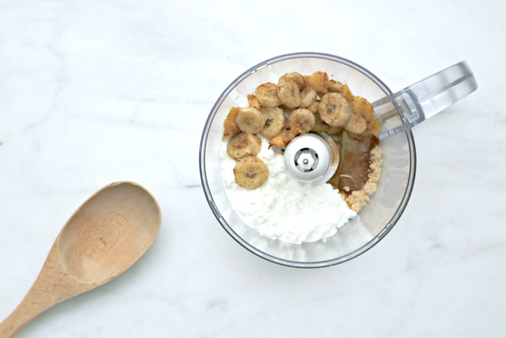 Roasted fruits, sugar, syrup, and cottage cheese being blended in a food processor.