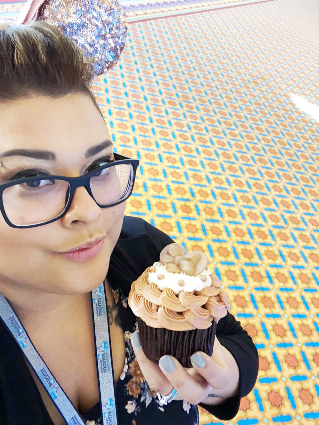 A woman holds a rose gold cupcake while wearing rose gold Minnie ears.