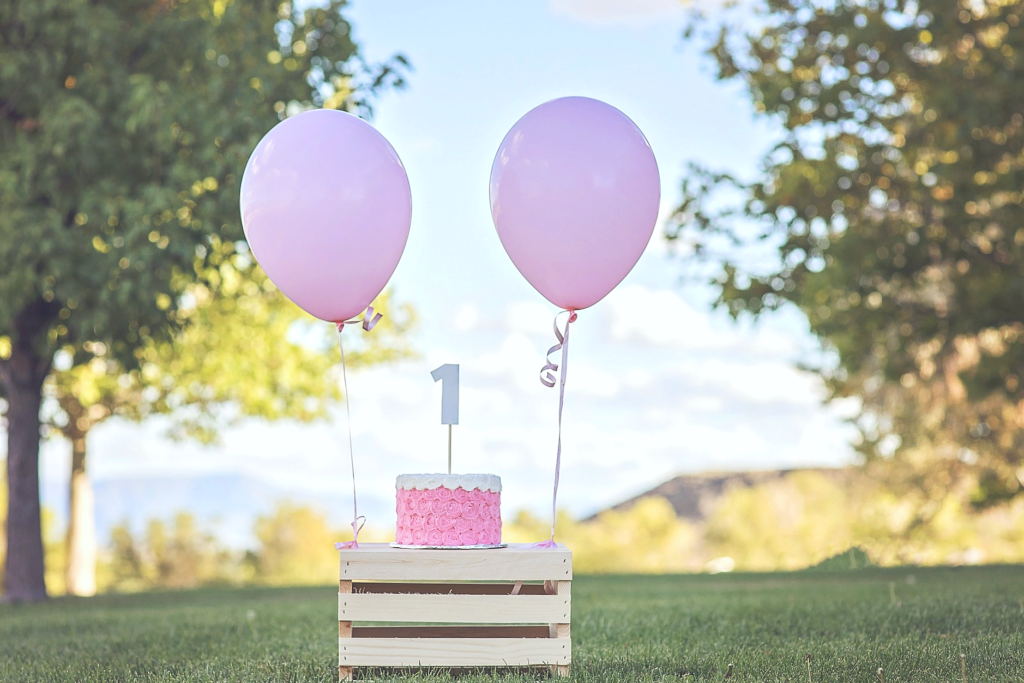 A crate holds a child's Birthday cake with two pink balloons tied to it. This article covers budget-friendly birthday party ideas for kids.