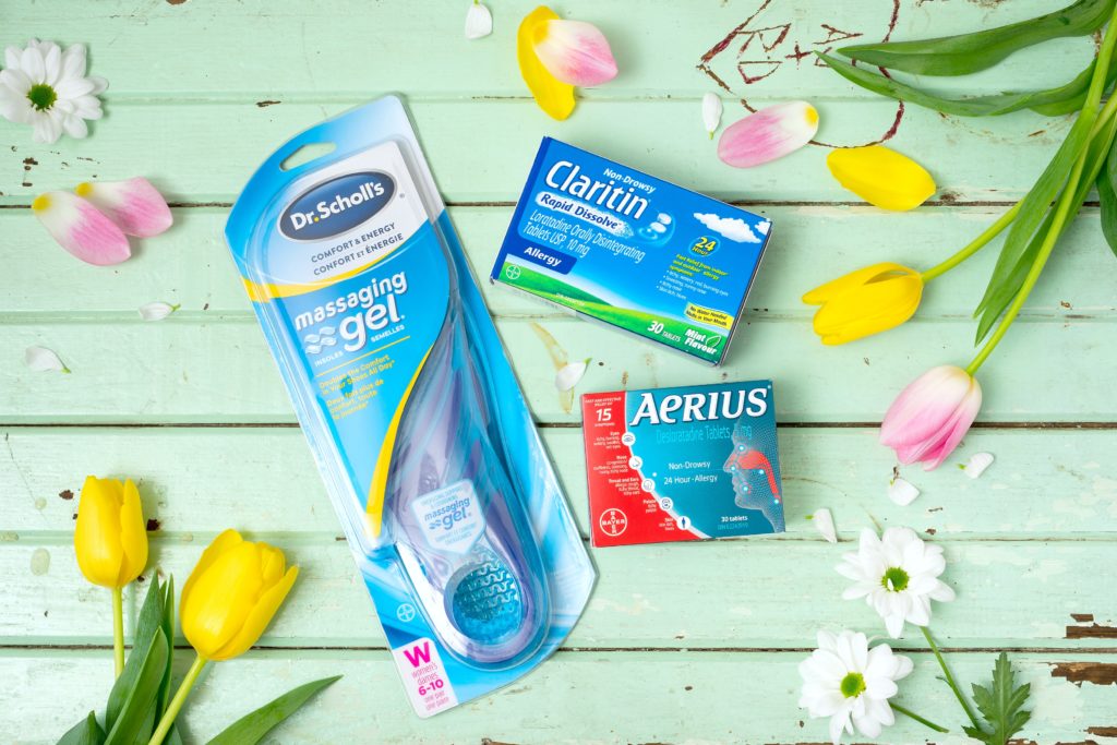 A teal wooden table with Dr. Scholl's insoles, a box of Claritin and Aerius with flowers strewn about.