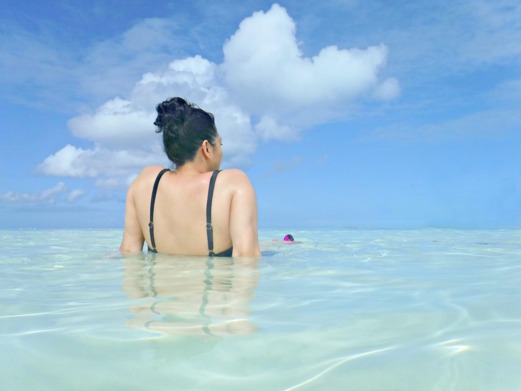 A woman sits in the water in the Bahamas, reflecting over the horizon.