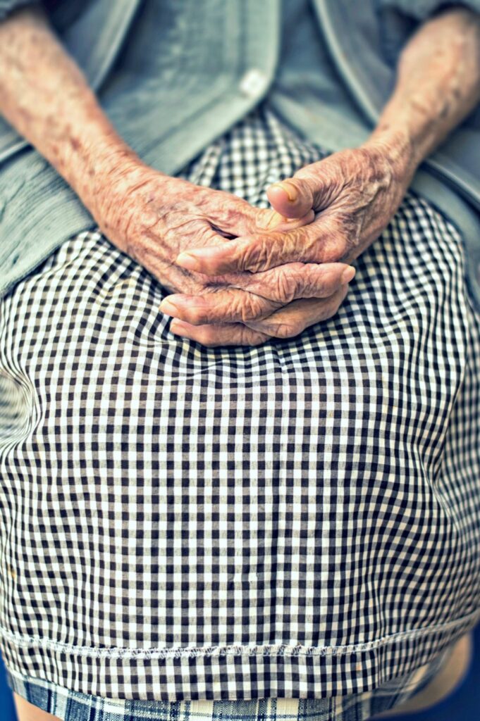 Older person sitting with fingers intertwined on lap.