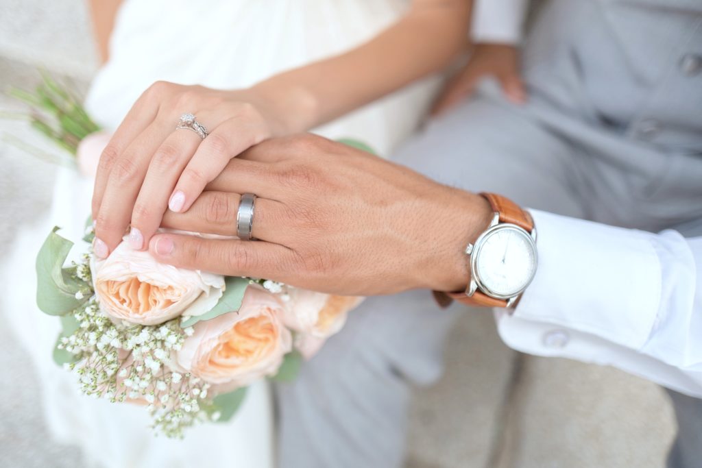 A man and woman hold hands over a bouquet on their wedding day.