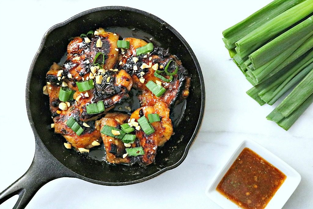 Skillet is shown topped with green onions and peanuts and extra sauce on the side. 
