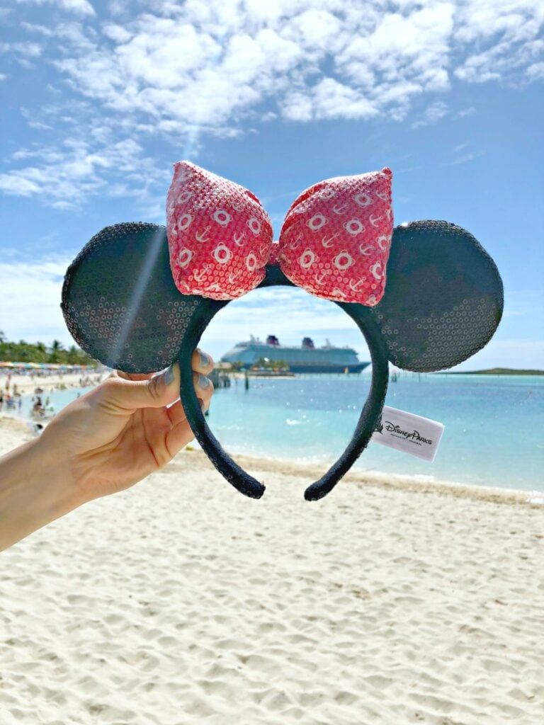 A woman holds up Disney Cruise Line Minnie ears and frames the Disney Cruise Ship, the Dream.