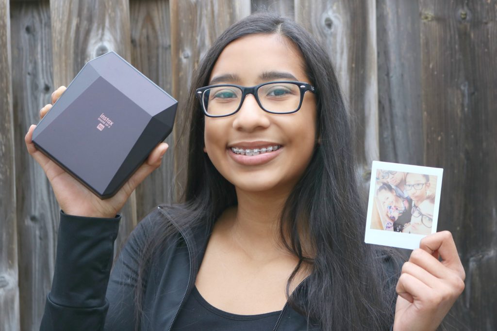 A teen girl holds up the FujiFilm Instax Square Share SP-3 printer with a printed picture.