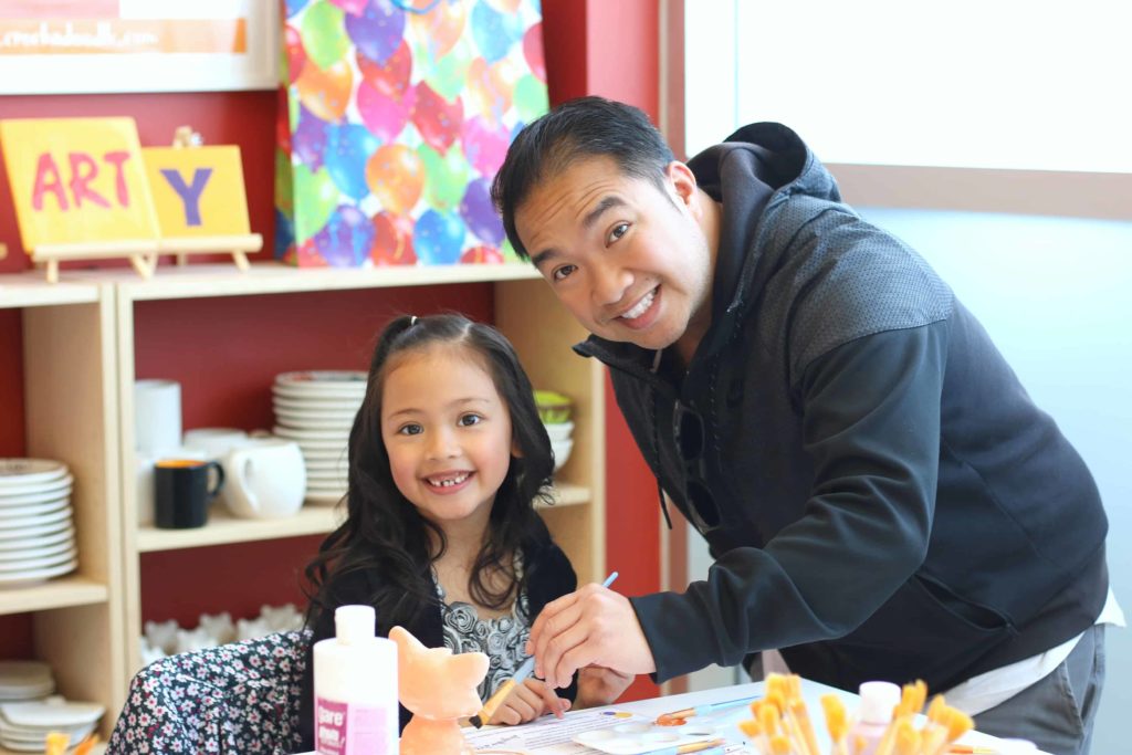 A dad helps his little girl fix a mistake on her pottery piece. 