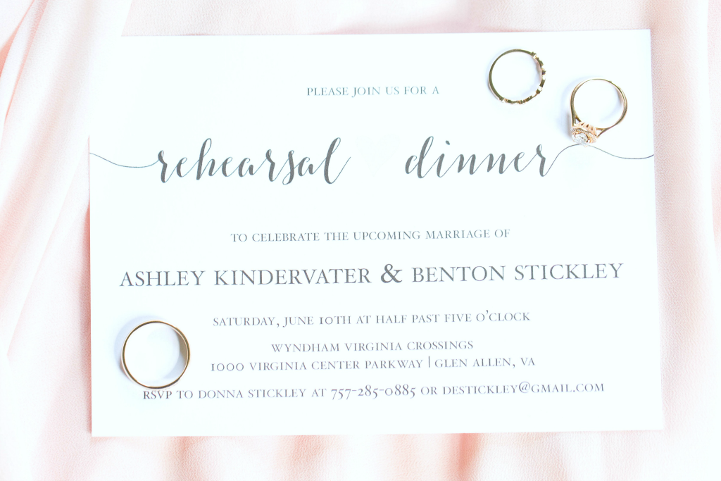 His and her rings are on top of a rehearsal dinner invitation.