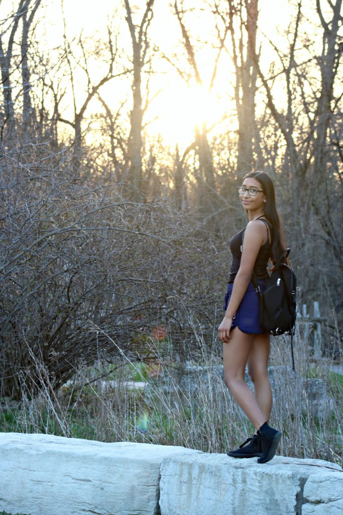 A teen girls stands on rocks and looks at the camera. 